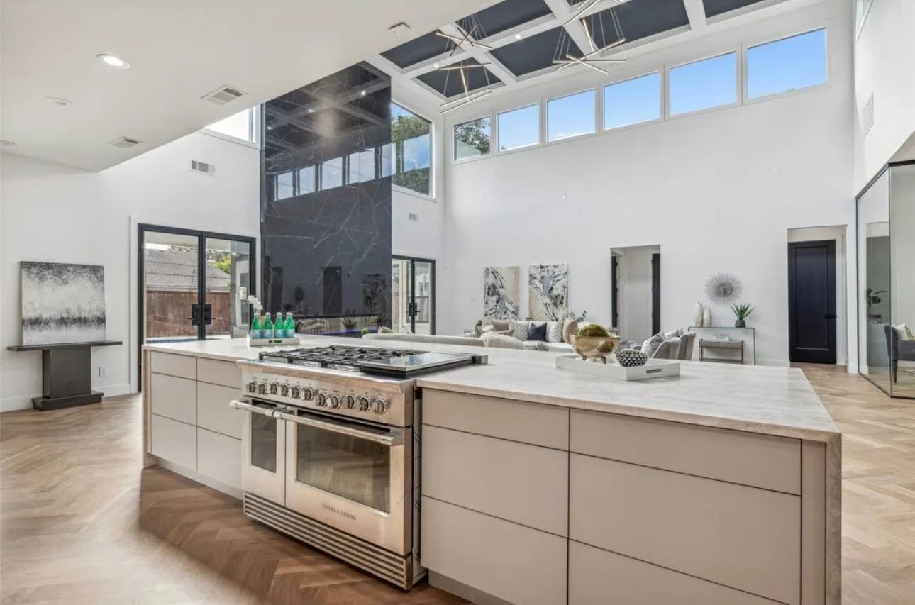 Modern kitchen with white cabinetry, stainless steel range, and open living area with skylights