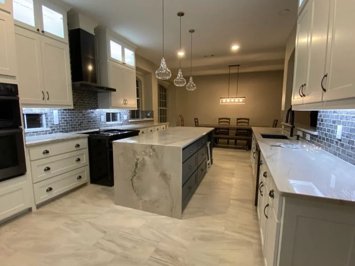 Modern kitchen with white cabinets, polished concrete floors, marble island, and blue tile backsplash